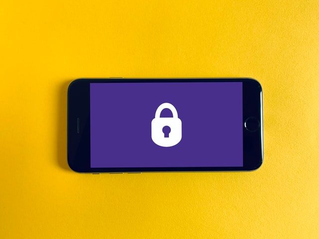 Iphone with a purple screen and a white padlock on a bright yellow background.
