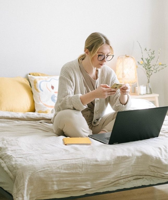 Woman wearing glasses sitting on her bed with a cup of coffee and her laptop computer searching for CIPP certifications