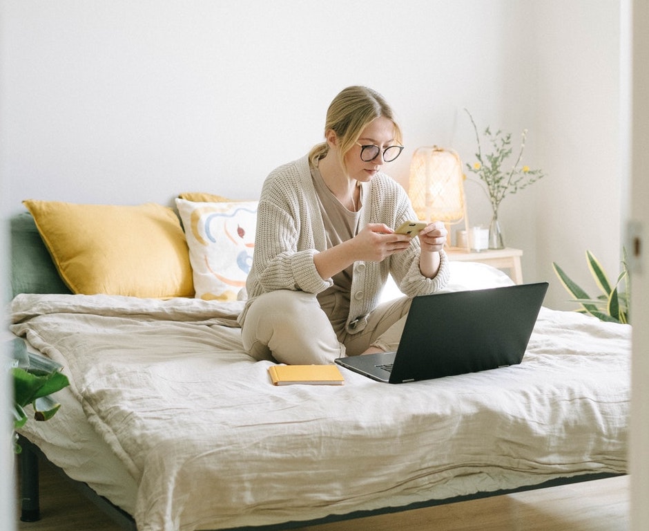 Woman wearing glasses sitting on her bed with a cup of coffee and her laptop computer searching for CIPP certifications