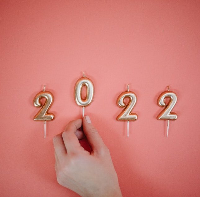 Pink background with gold candles spelling out 2022 and a hand placing the 0 candle in place to conceptualise the coming of the new year and the time to set privacy resolutions for businesses in 2022